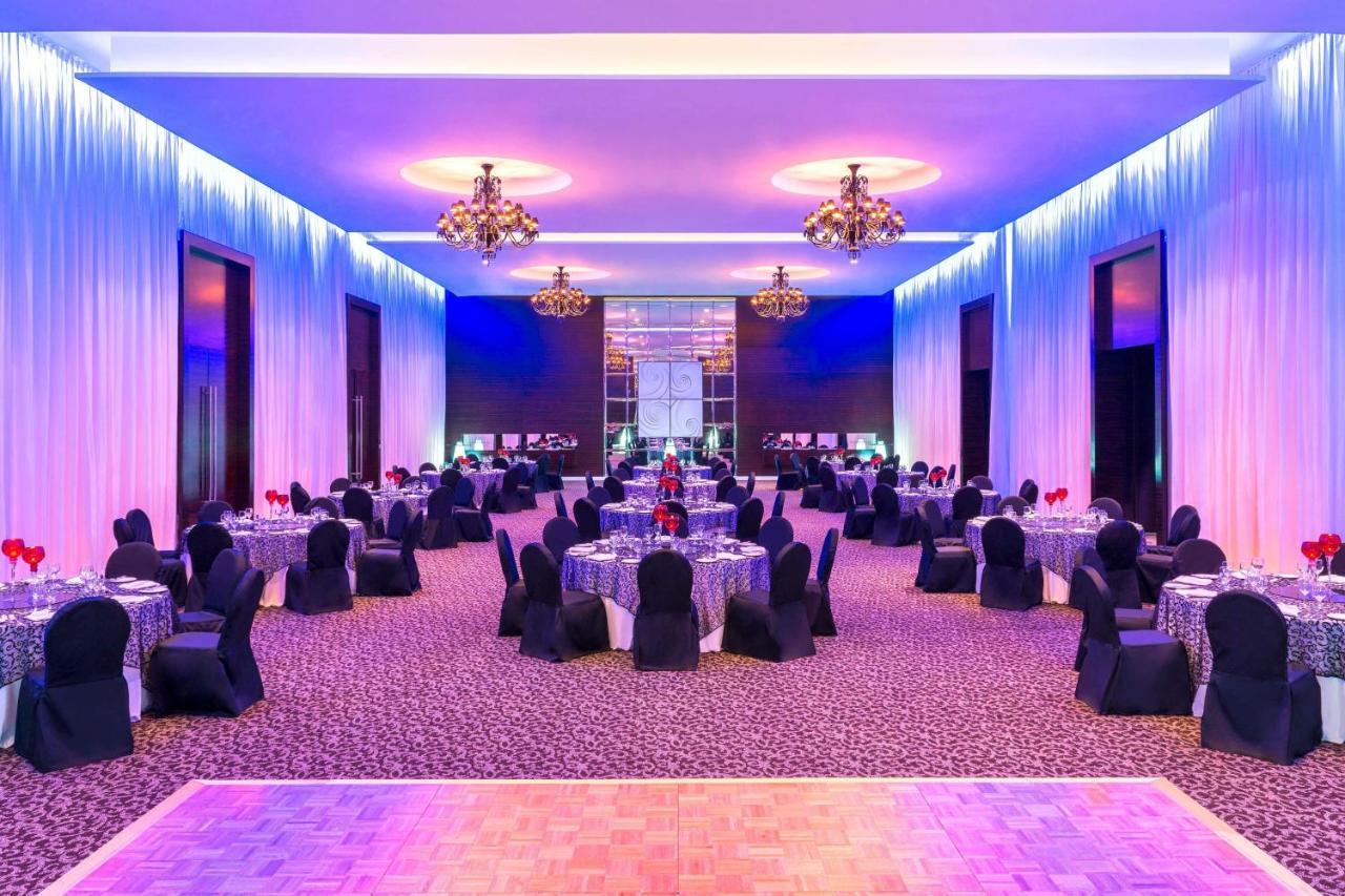 Le Meridien Dubai Hotel & Conference Centre Exterior photo The photo shows a spacious and elegantly decorated banquet hall. The room features several round tables, each set with tablecloths and adorned with centerpieces, likely for an event or celebration. The chairs are covered in black fabric, adding to th